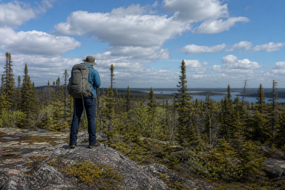 Hiker on a rocky boreal trail near Yellowknife pausing to scan the treeline on a bright summer day