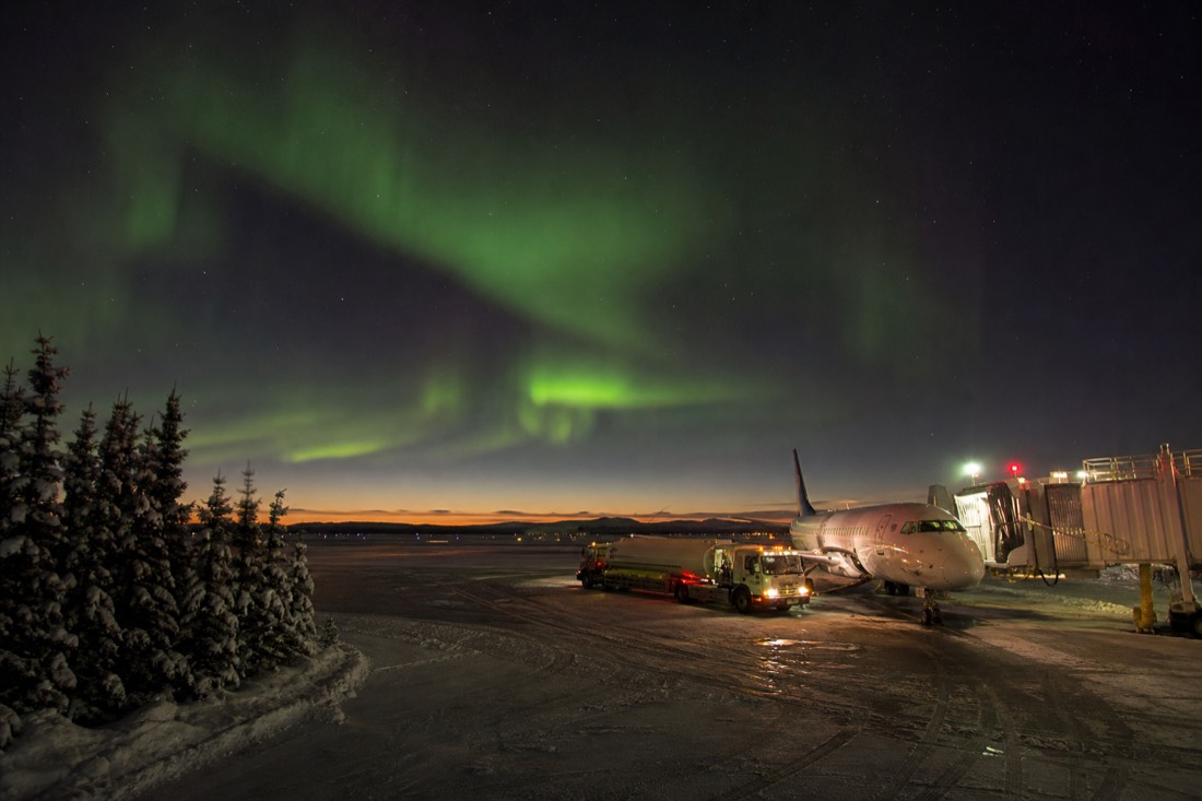 Regional jet parked at a northern airport gate with a fuel truck alongside and pink low winter light on the horizon