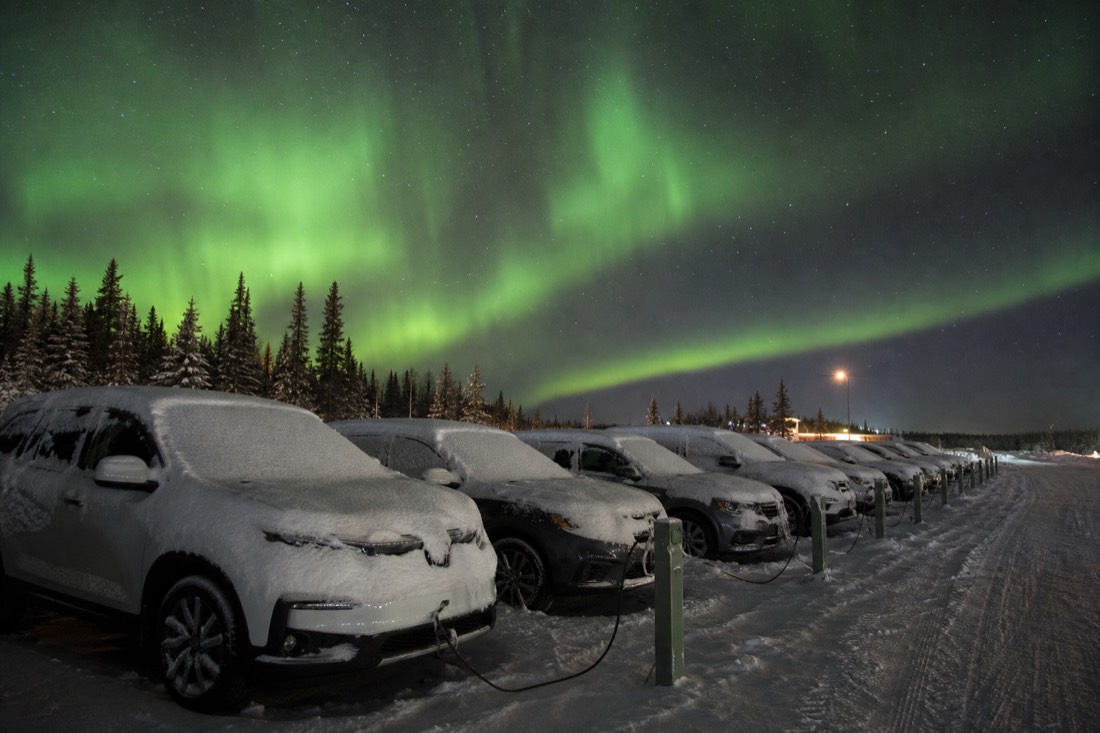 Row of snow-covered rental cars in a northern airport lot with block heater cords running to plug-in posts