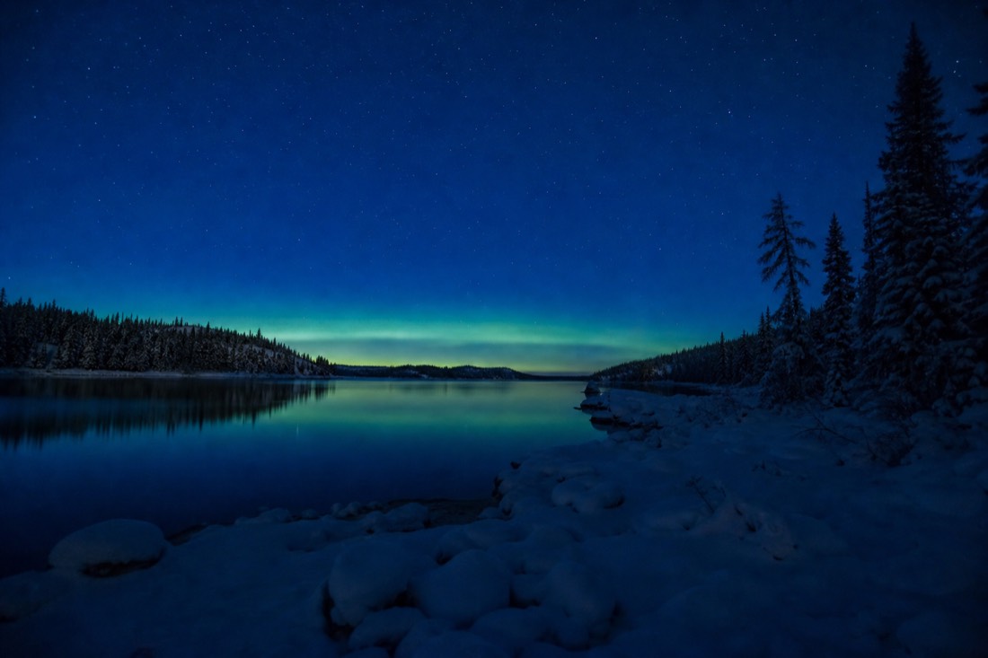 Deep blue late-August twilight over a calm northern lake with the first faint green band low on the horizon