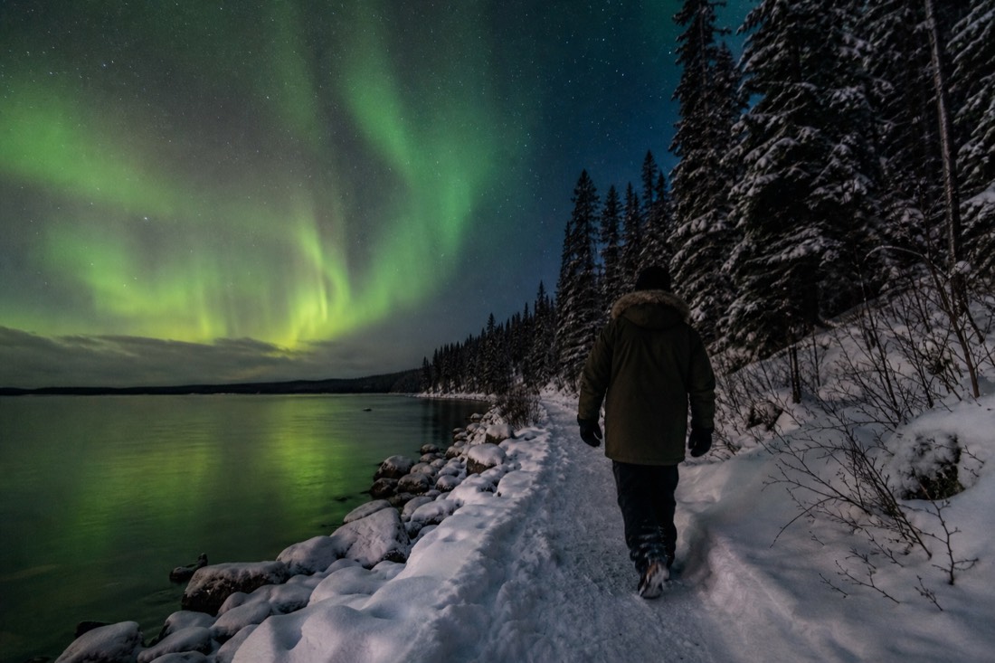 Walker in a heavy parka on a snow-packed lakeside path under low golden winter light