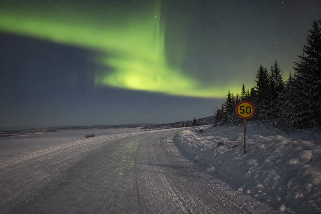 Speed limit sign planted in a snowbank beside an ice road with tire tracks curving past it