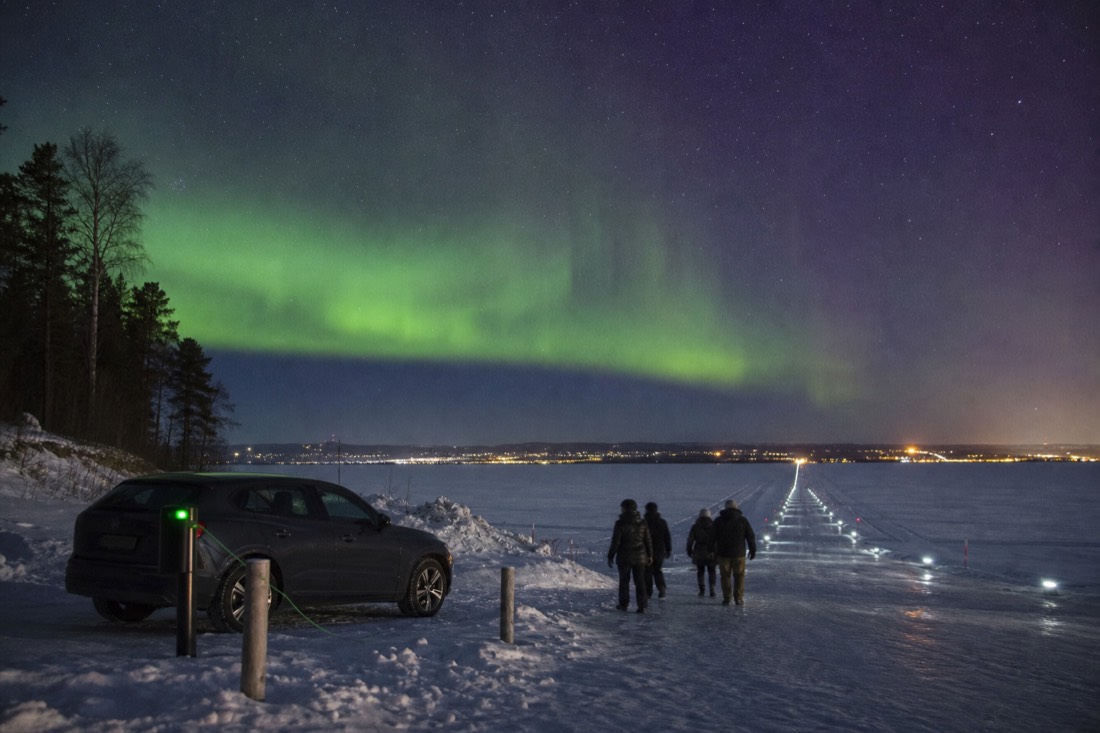 Visitors walking onto a marked ice road from the Old Town shore with a parked car plugged in nearby