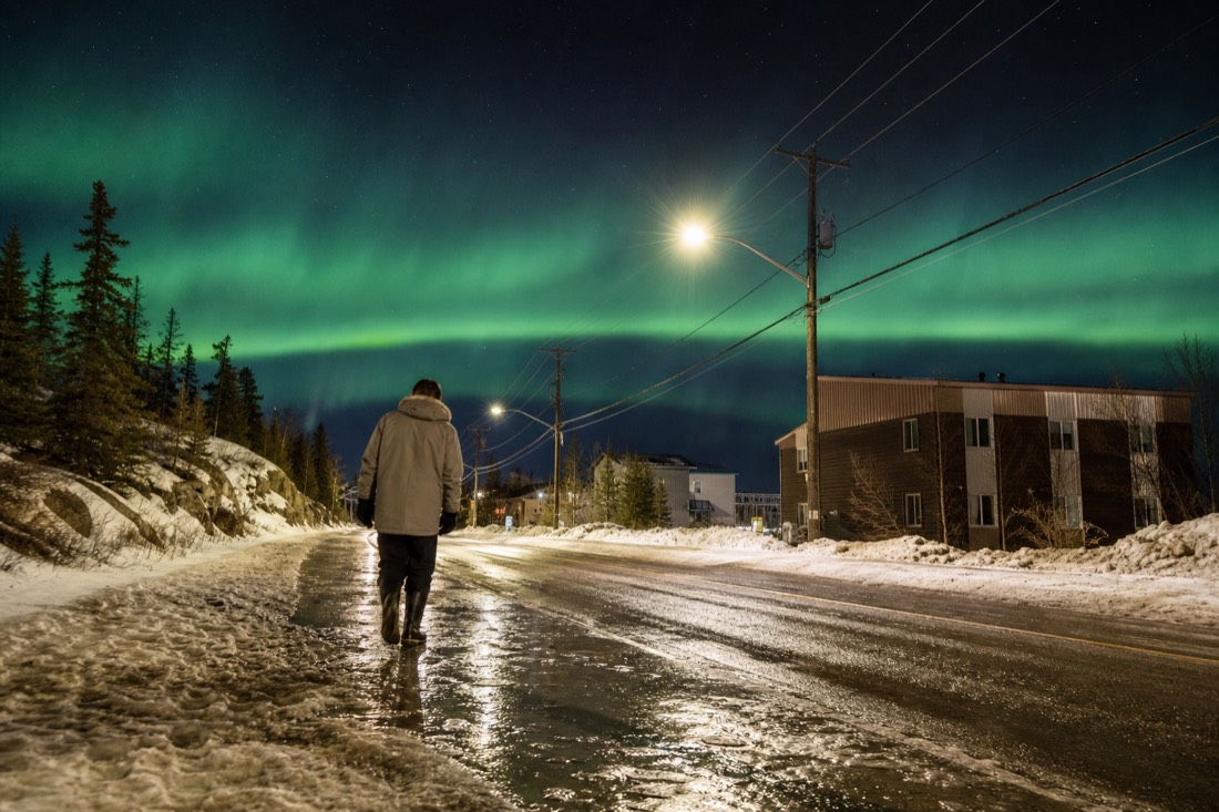 Traveler in a light parka and waterproof boots crossing slushy melting snow on a Yellowknife street in April