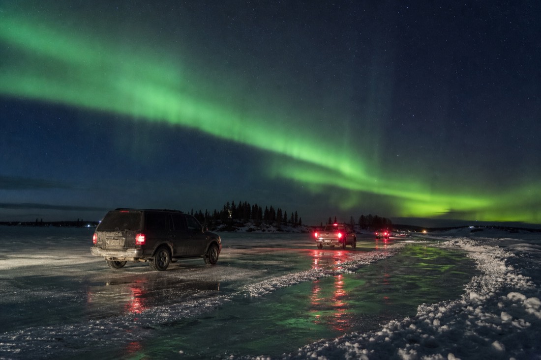 Cars on the Dettah ice road across Yellowknife Bay in April with meltwater pooling on the ice surface