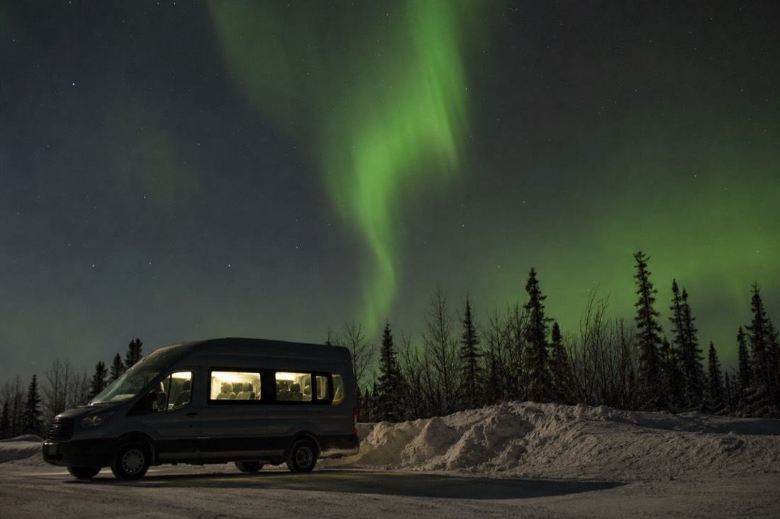 Small tour van parked beside a snowbank in Yellowknife at night with its interior lights on