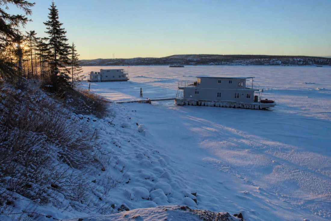 Frozen Yellowknife Bay in low February afternoon sun with houseboats locked in the ice and long blue shadows