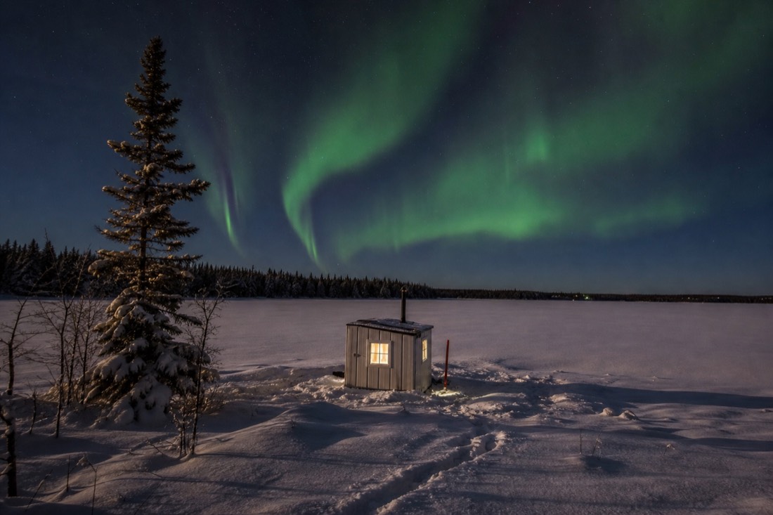 Heated ice fishing hut on a snow-covered frozen lake under low golden February afternoon light