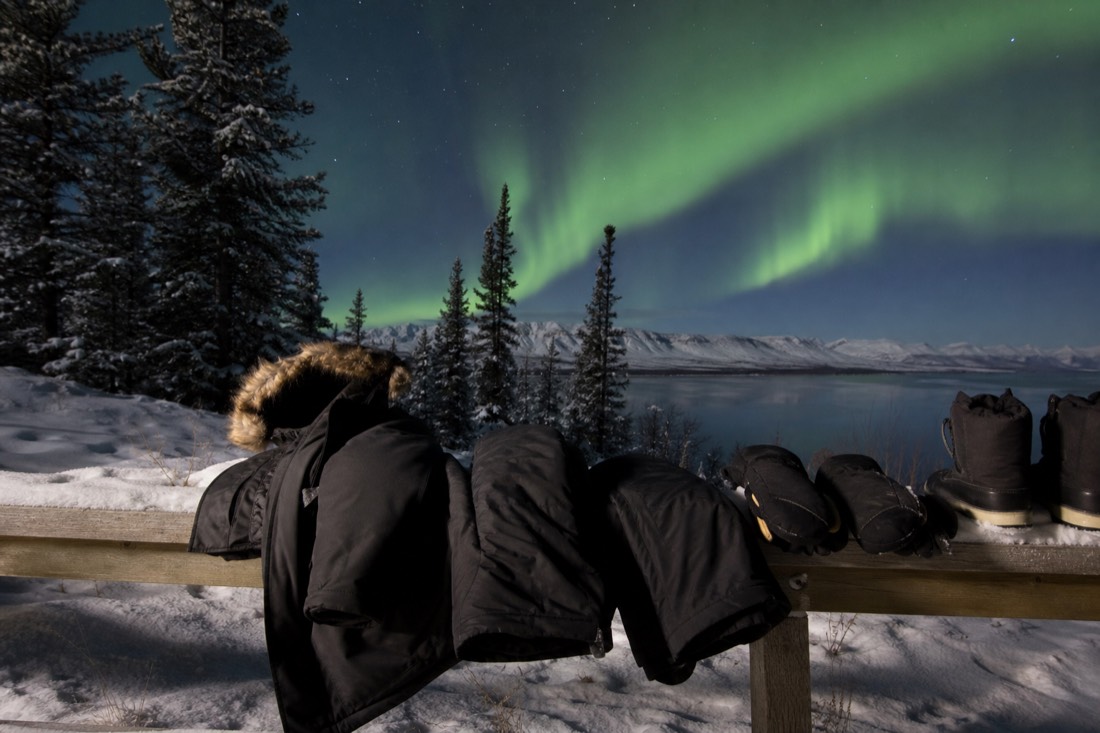 Rented arctic parka, insulated pants, mitts and heavy boots laid out on a bench before a January aurora tour