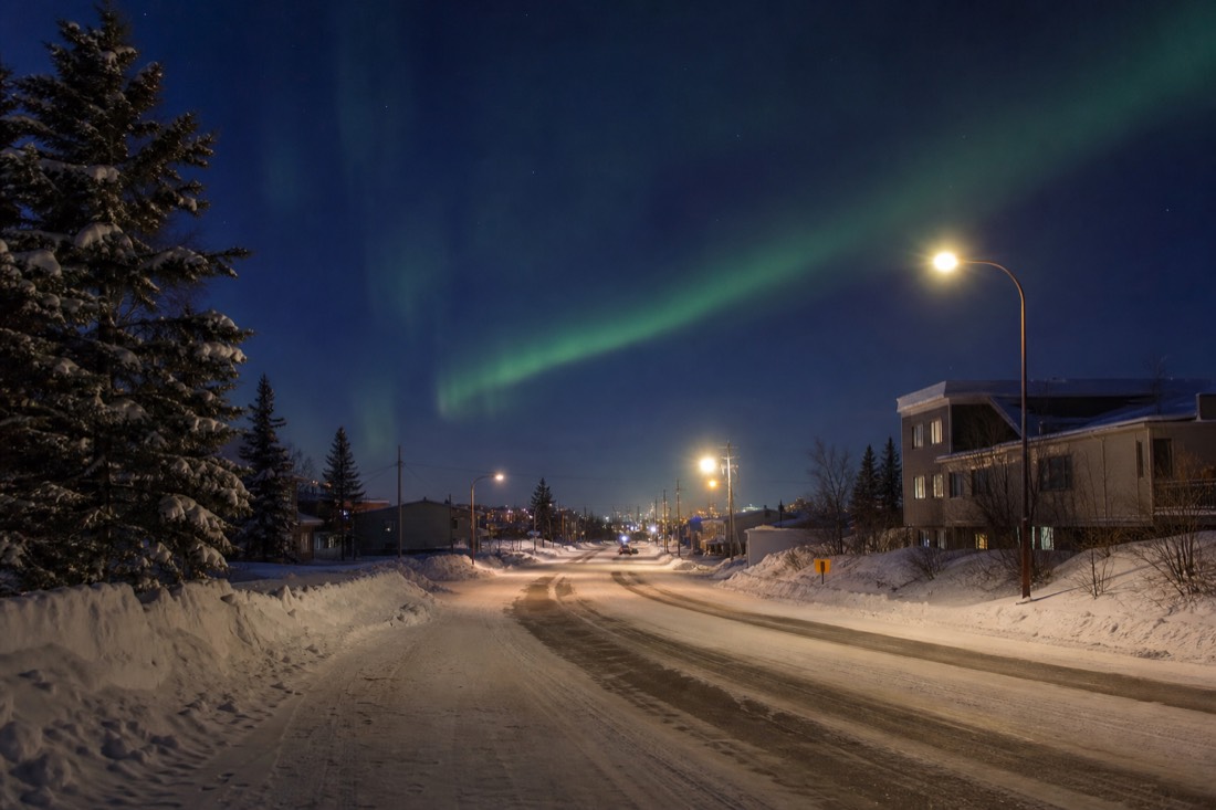 Deep blue late afternoon twilight over a snow-covered Yellowknife street with streetlights already on