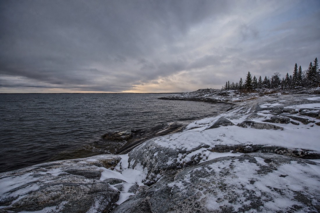 Bare granite shoreline and dark open water on Yellowknife Bay under a low grey October sky