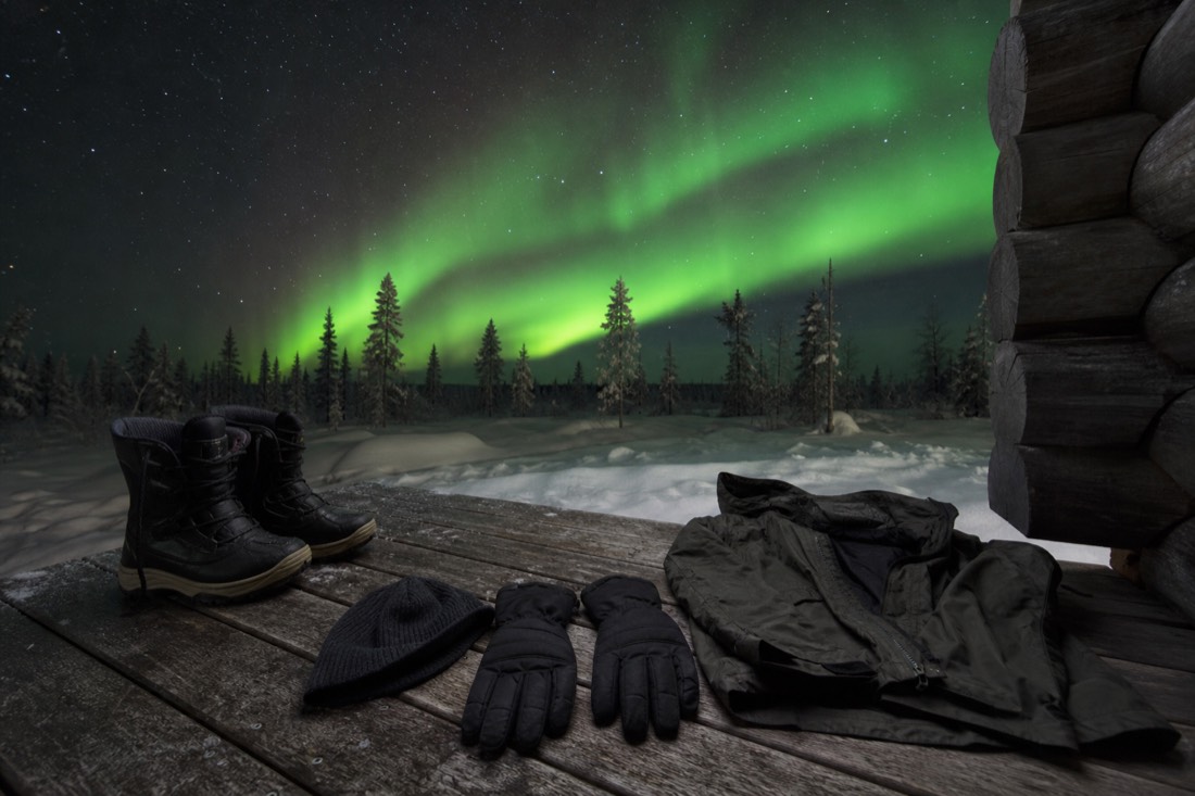 Insulated boots, gloves, a hat and a wind shell laid out on a wooden cabin floor
