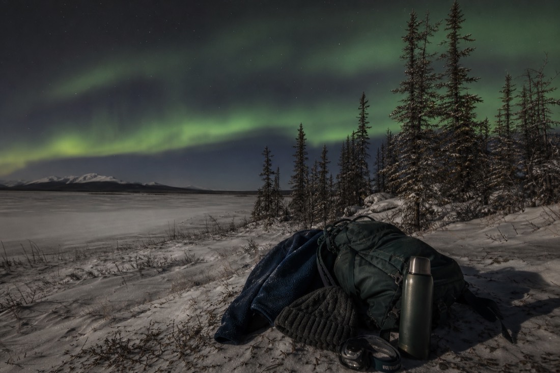 Backpack with a fleece, beanie, thermos, and headlamp laid out for a mild autumn aurora night