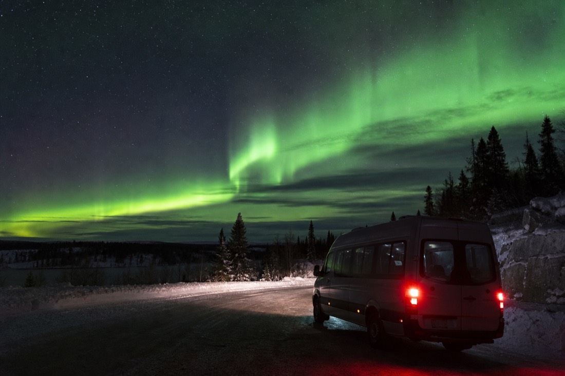 Aurora tour van parked on a dark road outside Yellowknife with green northern lights overhead